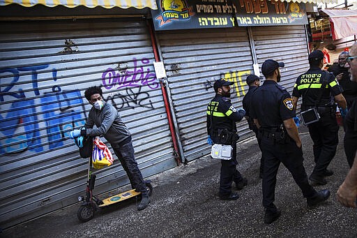 Israeli police officers order owners to shut down their shops in order to reduce the spread of the coronavirus, at a food market in Tel Aviv, Israel, Sunday, March 22, 2020. (AP Photo/Oded Balilty)