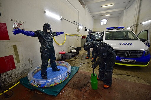 Volunteer workers of Search and Rescue (SAR) with special equipment, disinfect a volunteer after disinfecting a police car at Local Police station to prevent the spread of coronavirus COVID-19, in Pamplona, northern Spain, Sunday, March 22, 2020. For some people the COVID-19 coronavirus causes mild or moderate symptoms, but for some it causes severe illness. (AP Photo/Alvaro Barrientos)