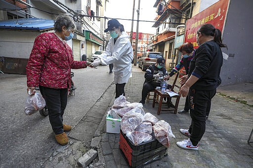 In this March 18, 2020 photo, people buy pork at the entrance gate of a closed residential community in Wuhan in central China's Hubei Province. Last month, Wuhan was overwhelmed with thousands of new cases of coronavirus each day. But in a dramatic development that underscores just how much the outbreak has pivoted toward Europe and the United States, Chinese authorities said Thursday that the city and its surrounding province had no new cases to report. The virus causes only mild or moderate symptoms, such as fever and cough, for most people, but severe illness is more likely in the elderly and people with existing health problems. (Chinatopix via AP)