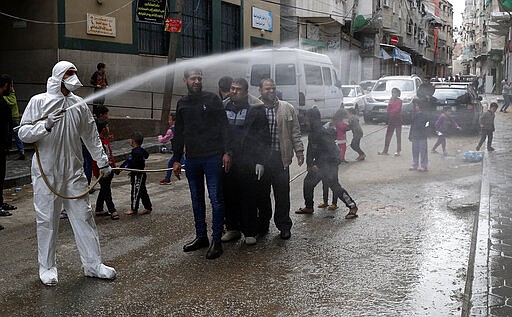 A worker wearing protective gear sprays disinfectant as a precaution against the coronavirus, in Gaza City, Thursday, March 19, 2020. The Middle East has some 20,000 cases of the virus, with most cases in Iran or linked to travel from Iran. The vast majority of people recover from COVID-19. (AP Photo/Adel Hana)