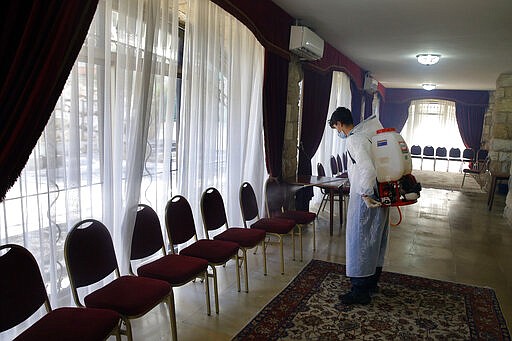 A municipal worker wearing protective gear sprays spray disinfectant as a precaution against the coronavirus, at a church in Beirut, Lebanon, Sunday, March 22, 2020. Lebanon has been taking strict measures to limit the spread of COVID-19 closing restaurants and nightclubs as well as schools and universities. (AP Photo/Bilal Hussein)