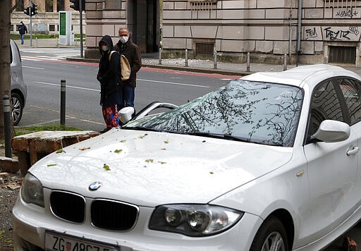 People inspect a car crushed by falling debris after an earthquake in Zagreb, Croatia, Sunday, March 22, 2020. A strong earthquake shook Croatia and its capital on Sunday, causing widespread damage and panic. (AP Photo/Darko Bandic)
