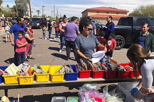 Parents of students at Encanto Elementary in Phoenix line up on Monday, March 23, 2020, to get packets of exercises for children to do at home. Like many schools across the nation, schools in Arizona have been ordered closed amid the coronavirus outbreak. (AP Photo/Peter Prengaman)