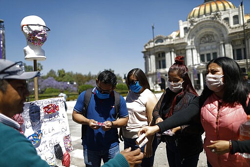 Customers purchase homemade fabric face masks being sold for 20 pesos (around 85 cents) from Jorge Rodriquez, on a street in Mexico City, Monday, March 23, 2020. Rodriguez said he was recently laid off from his construction job until further notice, and that he and his wife began making and selling the masks that people are using as a precaution to help stop the spread of the new coronavirus. (AP Photo/Rebecca Blackwell)