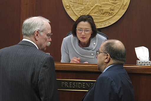 Alaska Senate President Cathy Giessel, center, speaks with Sens. Bert Stedman, left, and Lyman Hoffman, right, on the floor of the Senate on Monday, March 23, 2020, in Juneau, Alaska. The Senate on Monday debated a state spending package. (AP Photo/Becky Bohrer)