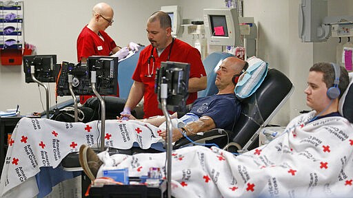 Eric Timpson, center, and Thomas Nicolaysen, right, give blood at the American Red Cross Donation Center Monday, March 23, 2020, in Murray, Utah. The U.S. surgeon general on Thursday, March 19, 2020, urged healthy Americans, especially younger ones, to donate blood as supplies dwindle amid the coronavirus outbreak. The industry has counted more than 12,000 blood drives canceled, some immediately and others set for coming months. (AP Photo/Rick Bowmer)