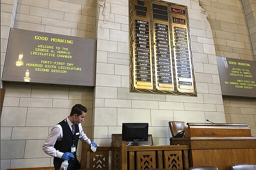 Ashton Krebs, a legislative page and University of Nebraska-Lincoln sophomore, wipes down the Nebraska Legislature's chamber on Monday, March 23, 2020, in advance of lawmakers temporarily reconvening to approve emergency funding to help the state's response to the new coronavirus in Lincoln, Neb. Legislative staffers are taking special precautions to keep the virus from spreading, such as allowing lawmakers to cast their vote from the back of the chamber to maintain distance from one another. (AP Photo/Grant Schulte).