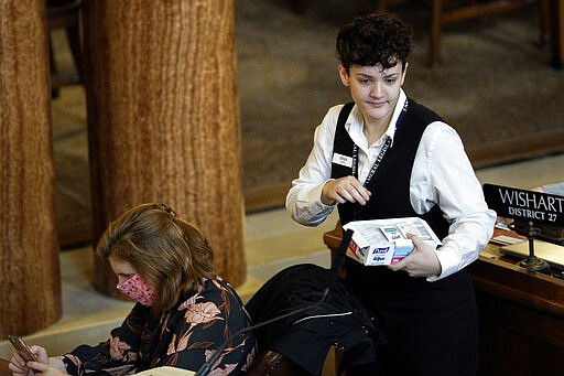 Erika, a legislativ page at the State Capitol in Lincoln, Neb., distributes sanitizing wipes to state senators including to Sen. Machaela Cavanaugh of Omaha, left, on Monday, March 23, 2020. Nebraska lawmakers reconvened on Monday to pass emergency funding for the coronavirus outbreak. (AP Photo/Nati Harnik)