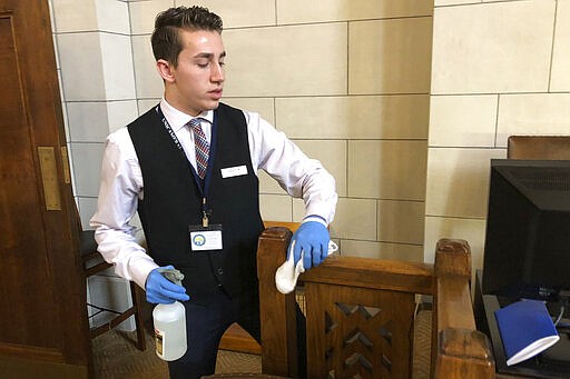 Ashton Krebs, a legislative page and University of Nebraska-Lincoln sophomore, wipes down the Nebraska Legislature's chamber on Monday, March 23, 2020, in advance of lawmakers temporarily reconvening to approve emergency funding to help the state's response to the new coronavirus in Lincoln, Neb. Legislative staffers are taking special precautions to keep the virus from spreading, such as allowing lawmakers to cast their vote from the back of the chamber to maintain distance from one another. (AP Photo/Grant Schulte).