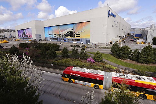 A bus drives past a Boeing airplane manufacturing plant, where murals of jets cover the massive doors, Monday, March 23, 2020, outside Seattle, in Renton, Wash. Boeing is suspending operations at its Seattle area facilities due to the spread of coronavirus in the area, where dozens of people have died. Operations would be reduced beginning Wednesday, the company said in a statement, and production would be suspended for a two weeks. (AP Photo/Elaine Thompson)