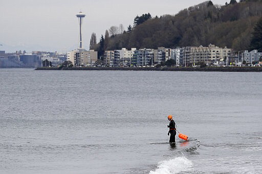 A swimmer enters the Puget Sound at Alki Beach Park Sunday, March 22, 2020, in Seattle, where people are asked to maintain a physical distance of at least six feet apart in response to the coronavirus outbreak. Health officials reported Sunday that there have been at least 95 coronavirus deaths in Washington state and nearly 2,000 confirmed cases. (AP Photo/Elaine Thompson)