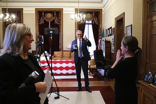 Washington Gov. Jay Inslee, center, maintains physical distance as he gives a thumbs-up in thanks to American Sign Language interpreters who interpreted for him as he spoke about additional plans to slow the spread of coronavirus in a televised address from his office Monday, March 23, 2020, in Olympia, Wash. The latest update from the Washington state Department of Health showed there have been at least 110 coronavirus deaths in the state and more than 2,200 confirmed cases. (AP Photo/Elaine Thompson)