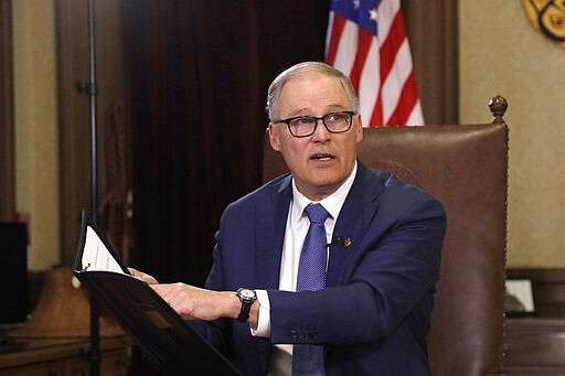 Gov. Jay Inslee turns to staff members as he prepares to speak about additional plans to slow the spread of coronavirus before a televised address from his office Monday, March 23, 2020, in Olympia, Wash. (AP Photo/Elaine Thompson)