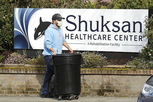 A worker wearing a mask walks past a sign near the entrance of the Shuksan Healthcare Center in Bellingham, Wash., Monday, March 23, 2020. The skilled nursing center had 29 new cases of the new coronavirus confirmed on Sunday in both residents and employees according to the Whatcom County Health Department. (AP Photo/Ted S. Warren)