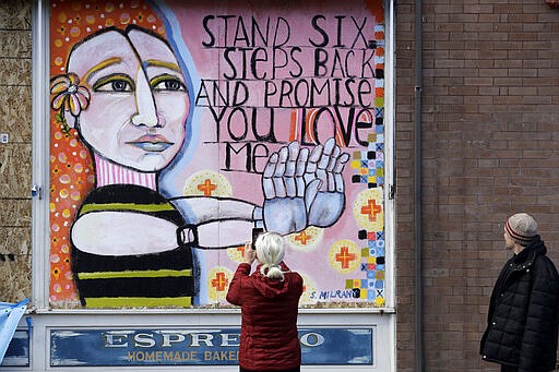 A pedestrian stops to take a photo of a closed and boarded-up restaurant decorated with artwork in response to the coronavirus outbreak, Monday, March 23, 2020, in Seattle. The state has already closed schools through late April, banned events and large gatherings and ordered bars to close and restaurants to serve only take out or delivery options and state and local leaders continue to urge people to stay at home and practice social distancing. (AP Photo/Elaine Thompson)