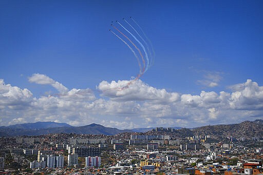 Military planes trail colored smoke as they fly in formation above the city of Caracas, Venezuela, Sunday, March 22, 2020. (AP Photo/Matias Delacroix)