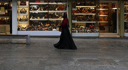 A woman wearing a face mask as a preventive measure against the spread of the new coronavirus walks past shoe shops in a mostly empty street in a commercial district in downtown Tehran, Iran, Sunday, March 22, 2020. on Sunday, Iran imposed a two-week closure on major shopping malls and centers across the country to prevent spreading the virus. Pharmacies, supermarkets, groceries and bakeries will remain open. (AP Photo/Vahid Salemi)