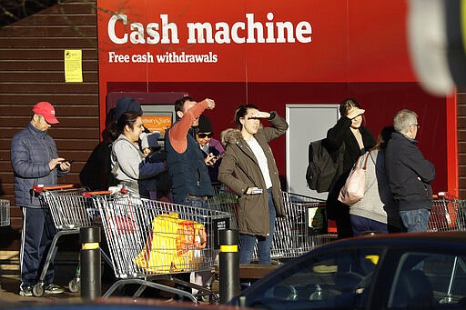 A queue of people wait outside Sainsbury's supermarket in front of a Coronavirus information display as National Health Service staff and social care workers who show their NHS ID are allowed into a branch of Sainsbury's supermarket 30 minutes before other customers who are made to wait outside the store, at the start of stores trading day in Kingston Upon Thames, south west London, Monday, March 23, 2020. This is to help NHS staff many of whom work shift patterns to buy food and other essentials, as they treat a rising number of Covid-19 patients, the supermarket chain will run this ongoing service Monday to Saturday, throughout Britain. Other supermarket chains are doing similar services for NHS staff. For most people, the new coronavirus causes only mild or moderate symptoms, such as fever and cough. For some, especially older adults and people with existing health problems, it can cause more severe illness, including pneumonia. These people are not members of the NHS staff and wait in line for the store to let them enter at the correct time.(AP Photo/Matt Dunham)