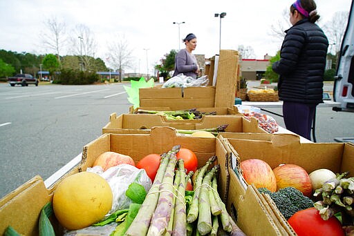 Anna Sullivan, right, helps a customer at a makeshift farm stand in the parking lot of a closed supermarket in Wake Forest, N.C., on Sunday, March 22, 2020. Lyons Farms would normally be at the farmers' market in nearby Durham, but it's been closed due to the Coronavirus pandemic. Sullivan made up pre-packed $20 boxes for people who might be worried about handling the produce. (AP Photo/Allen G. Breed)