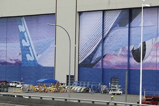 A worker walks near a mural of a Boeing 777 airplane at the company's manufacturing facility in Everett, Wash., Monday, March 23, 2020, north of Seattle. Boeing announced Monday that it will be suspending operations and production at its Seattle area facilities due to the spread of the new coronavirus. (AP Photo/Ted S. Warren)