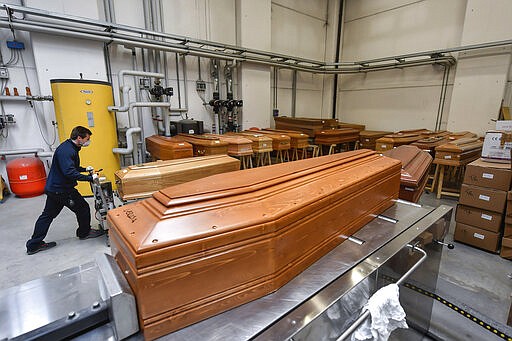 A worker takes in a coffin in the Crematorium Temple of Piacenza, Northern Italy, saturated with corpses awaiting cremation due to the coronavirus emergency Monday, March 23, 2020. For most people, the new coronavirus causes only mild or moderate symptoms. For some it can cause more severe illness, especially in older adults and people with existing health problems. (Claudio Furlan/LaPresse via AP)