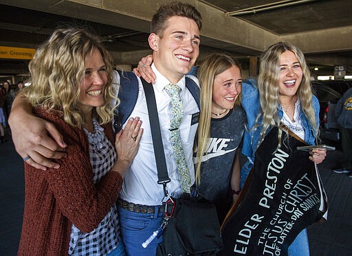 In this Sunday, March 22, 2020 photo, the Preston family from Kaysville, Utah, welcomes home Elder Kaleb Preston from his mission in the Philippines, at the Salt Lake City International Airport. Sen. Mitt Romney and Utah state leaders are criticizing a large gathering of family and friends who went to the Salt Lake City airport to welcome home missionaries when people are supposed to be keeping their distance from one another to prevent more spread of the coronavirus. (Rick Egan/The Salt Lake Tribune via AP)