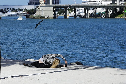 FILE - In this March 20, 2020 file photo, a woman works out near Bayfront Park amid the coronavirus outbreak in Miami. People around the country who are self-isolating or maintaining social distance during the coronavirus outbreak have to think outside the gym when it comes to their fitness routines. Many are turning to online classes or getting outside to exercise. (AP Photo/Brynn Anderson, File)