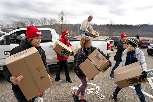 Kim Lutes left, a registered nurse and others carries boxes of N-95 masks donated by Rich Forstner president at Mavo Systems, Sunday, March 22, 2020 in St. Paul, Minn. Minnesota Nurses Association held drives collecting any spare certified N-95 medical masks from people that can be used by healthcare workers to protect themselves during the coronavirus outbreak in their parking lot. (Jerry Holt/Star Tribune via AP)