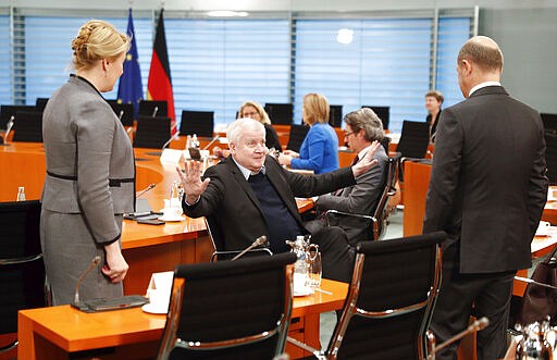 German Interior Minister Horst Seehofer, center, gestures to Finance Minister Olaf Scholz, right, and Minister for Family Affairs, Senior Citizens, Women and Youth Franziska Giffey, left, to keep a safe distance because of the coronavirus outbreak, prior to the weekly cabinet meeting at the chancellery in Berlin, Germany, Monday, March 23, 2020. (Fabrizio Bensch via AP/Pool)