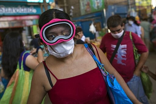 A woman wears a scuba mask and a surgical mask as a precaution against the spread of the new coronavirus, while buying food in a popular market in Lima, Peru, Monday, March 23, 2020. The vast majority of people recover from the COVID-19 disease. (AP Photo/Rodrigo Abd)