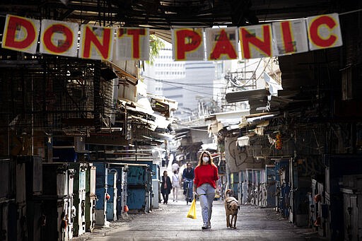 A woman walks her dog under a &quot;don't panic&quot; sign hanging on the entrance of a food market that was shut down in order to reduce the spread of the coronavirus, in Tel Aviv, Israel, Monday, March 23, 2020. In Israel daily life has largely shut down with COVID-19 cases multiplying greatly over the past week. (AP Photo/Oded Balilty)