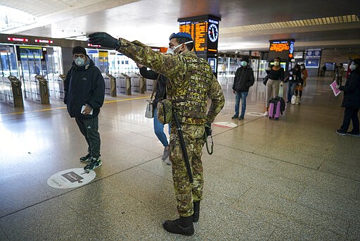 A soldier gives indications to passengers as they line up to have their travel documents checked, in Rome's Termini main train station, Monday, March 23, 2020. For most people, the new coronavirus causes only mild or moderate symptoms. For some it can cause more severe illness, especially in older adults and people with existing health problems.(AP Photo/Andrew Medichini)