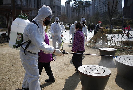 Members of a local residents group wear protective gear as they disinfect a local park as a precaution against the new coronavirus in Seoul, South Korea, Monday, March 23, 2020. For most people, the new coronavirus causes only mild or moderate symptoms. For some it can cause more severe illness. (AP Photo/Lee Jin-man)