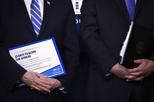 Vice President Mike Pence, left, and Attorney General William Barr hold binders as President Donald Trump speaks about the coronavirus in the James Brady Briefing Room, Monday, March 23, 2020, in Washington. (AP Photo/Alex Brandon)