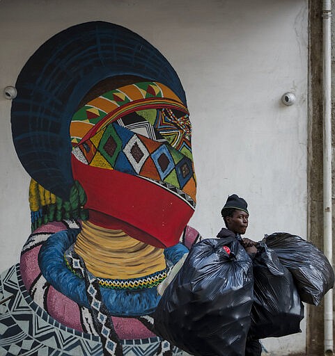 A man carrying plastic bags walks past a mural outside the Wits University school of art in Johannesburg, South Africa, Monday, March 16, 2020. South African President Cyril Ramaphosa declared a national state of disaster. Ramaphosa said all schools will be closed for 30 days from Wednesday and he banned all public gatherings of more than 100 people. South Africa will close 35 of its 53 land borders and will intensify screening at its international airports. For most people, the new COVID-19 coronavirus causes only mild or moderate symptoms. For some it can cause more severe illness. (AP Photo/Themba Hadebe)