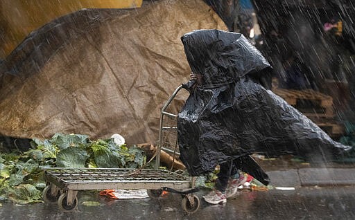 A man shelters from the rain with  plastic bags, at a market in Tembisa, east of Johannesburg, South Africa, Monday, March 23, 2020. South Africa, Africa's most industralized economy and a nation of 57 million people, will to go into a nationwide lockdown for 21 days from Thursday to fight the spread of the new coronavirus. (AP Photo/Themba Hadebe)