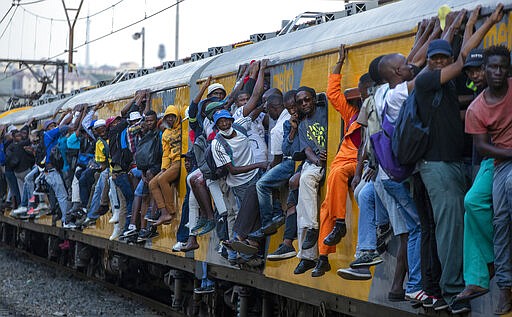 Train commuters hold on to the side of an overcrowded passenger train in Soweto, South Africa, Monday, March 16, 2020. South Africa will revoke nearly 10,000 visas issued this year to people from China and Iran, and visas will now be required for other high-risk countries that had been visa-free, including Italy and the United States. For most people, the new coronavirus causes only mild or moderate symptoms. For some it can cause more severe illness, especially in older adults and people with existing health problems.(AP Photo/Themba Hadebe)