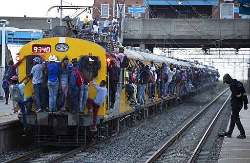 Train commuters hold on to the side of an overcrowded passenger train in Soweto, South Africa, Monday, March 16, 2020. South Africa will revoke nearly 10,000 visas issued this year to people from China and Iran, and visas will now be required for other high-risk countries that had been visa-free, including Italy and the United States. (AP Photo/Themba Hadebe)