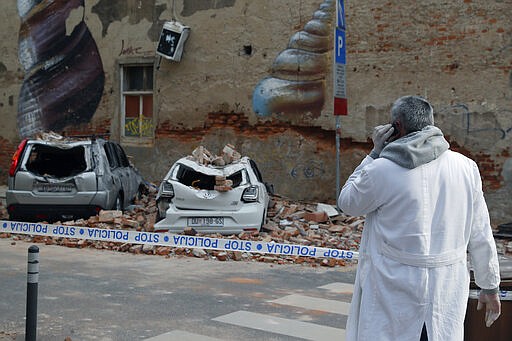 A man uses his phone as he looks at the damage after an earthquake, in downtown Zagreb, Croatia, Monday, March 23, 2020. Croatia experienced a series of aftershocks a day after a strong earthquake triggered widespread damage and injured over 20 people in the capital. (AP Photo/Darko Bandic)