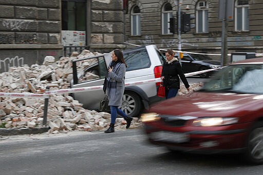 Pedestrians walk past a car damaged by the earthquake in downtown Zagreb, Croatia, Monday, March 23, 2020. Croatia experienced a series of aftershocks a day after a strong earthquake triggered widespread damage and injured over 20 people in the capital. (AP Photo/Darko Bandic)