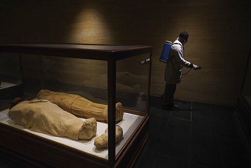 A worker disinfects around mummies in the hall of the Queens, in an effort to help prevent the spread of the coronavirus, at the Egyptian Museum in Tahrir Square, Cairo, Egypt, Monday, March 23, 2020. (AP Photo/Hamada Elrasam)