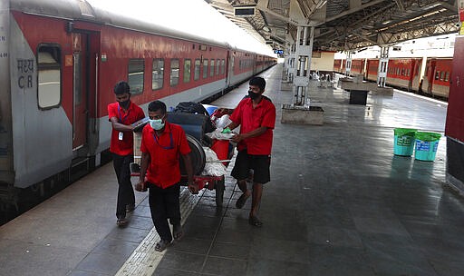 Railway workers wearing masks push a handcart at Lokmanya Tilak Terminus in Mumbai, India, Monday, March. 23, 2020. As India expanded its virus-containment measures and halted its lifeblood train network, the federal government warned Monday of strict legal action for those who flout the rules. (AP Photo/Rafiq Maqbool)