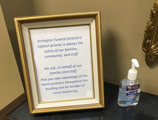 This March 19, 2020, photo provided by Bob Arrington of Arrington Funeral Directors shows a sign requesting visitors to use hand sanitizer and maintain social distancing amid the coronavirus outbreak, at their funeral home in Jackson, Tenn. (Cliff Walker Jr./Arrington Funeral Directors via AP)