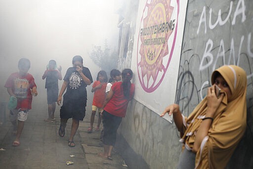 People cover their faces in a fog of fumigation to kill mosquitos to help prevent the outbreak of dengue fever in Jakarta, Indonesia, Monday, March 23, 2020. Indonesian President Joko Widodo has ruled out the possibility of imposing a lockdown on the capital city and has instead ordered mass testing to contain the coronavirus disease spread and has prepared about 200 hospitals run by government, military and police as well as private as the country braces for an anticipated surge in COVID-19 patients. (AP Photo/Dita Alangkara)