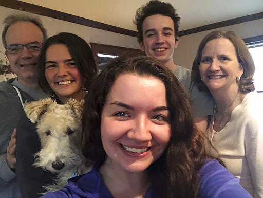 In this photo provided by Clare Sulentic, Sulentic, center, takes a family photo on Friday, March 20, 2020, at her parents' home in Dubuque, Iowa. Sulentic, 23, is a graduate student at St. Ambrose University. Like many students, she is taking classes online during the virus crisis. From left in back are her father, Bill Sulentic, sister Anna Sulentic, 21, brother John Sulentic, 18, and mother, Mary Sulentic. Missing from the photo is sister Maggie, who is hunkering down in Minneapolis. (Clare Sulentic via AP)