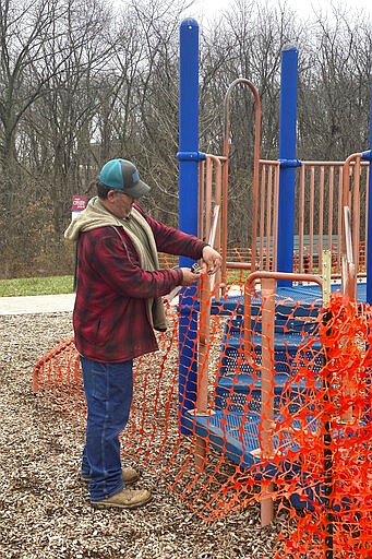 This Tuesday, March 24, 2020, photo provided by the City of Hannibal, Mo., Parks and Recreation Department employee Chad Hatton ropes off playground equipment at Huckleberry Park. The city is either removing or roping off all playground equipment, and is removing picnic tables from parks to  prevent the spread of coronavirus. (Mary Lynne Richards/The City of Hannibal via AP)