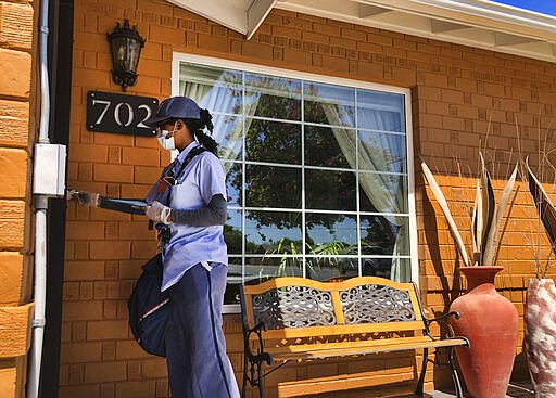 A mail worker in Phoenix wears a mask and gloves as she delivers mail on Tuesday, March 24, 2020. Schools have been closed and many businesses shuttered around the state amid the coronavirus outbreak. (AP Photo/Peter Prengaman)