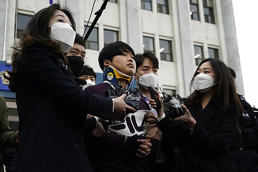 Cho Ju-bin, center, leader of South Korea's online sexual blackmail ring which is so called &quot;Nth room,&quot; is surrounded by journalists while walking out of a police station as he is transferred to prosecutors' office for further investigation in Seoul, South Korea, Wednesday, March 25, 2020. South Korean prosecutors on Wednesday began reviewing whether to formally charge a man arrested last week on allegations he operated secretive chatrooms where he posted sexually abusive videos of blackmailed women in return for cryptocurrency payments. (Kim Hong-Ji/Pool Photo via AP)