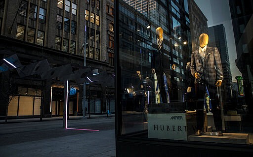 In this Monday, March 23, 2020, photo, mannequins in the window of Hubert White are seen at night with deserted streets during the coronavirus outbreak at Nicollet Mall in downtown Minneapolis. (Carlos Gonzalez/Star Tribune via AP)