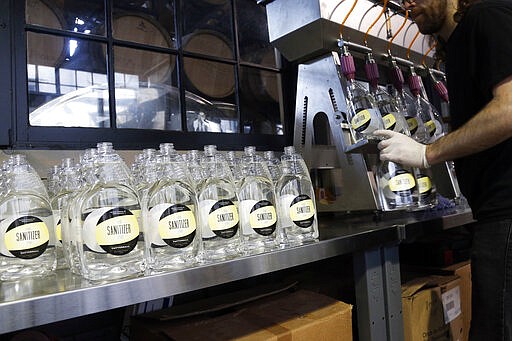 Bottles are filled with hand sanitizer at Tattersall Distilling Tuesday, March 24, 2020 in Minneapolis as the company lent an effort to provide the sanitizer, made from a World Health Organization recipe and signed off by the FDA, to make available for nursing homes, health centers and first responders fighting the coronavirus. (AP Photo/Jim Mone)